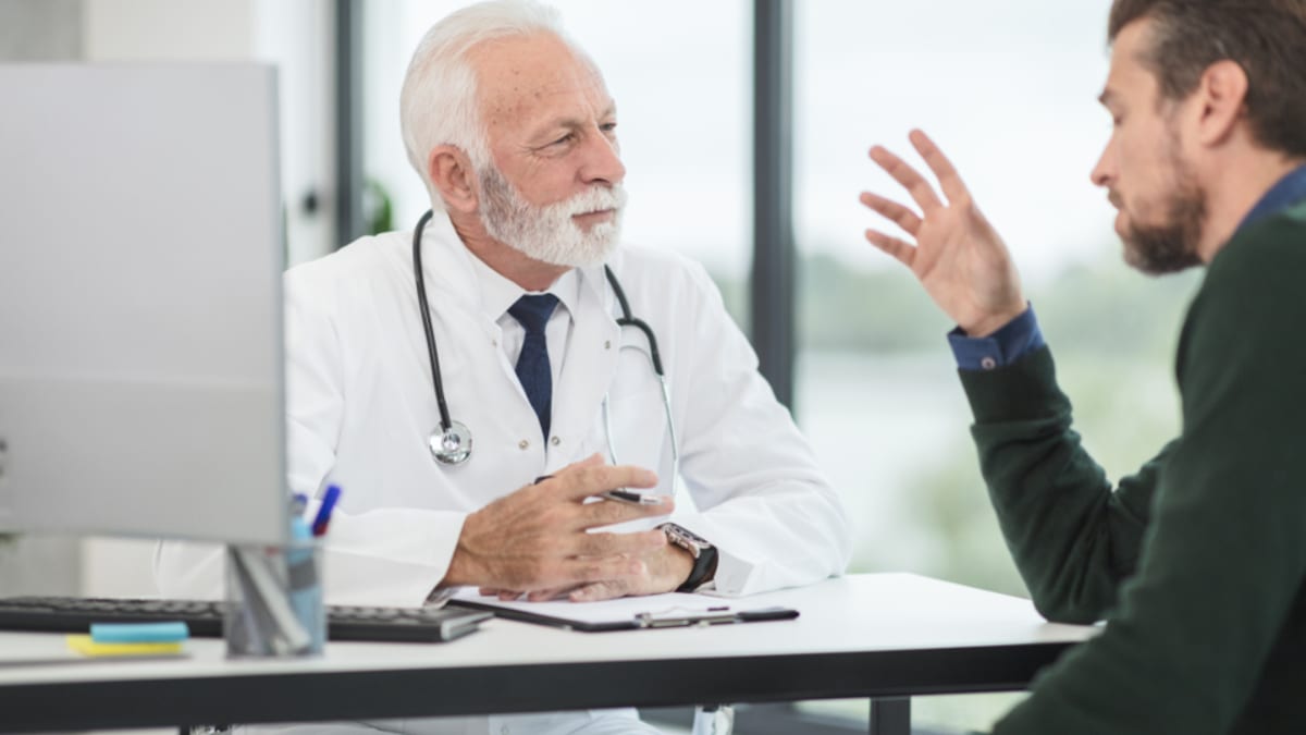 A doctor listens as a patient asks a question across his desk